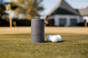 Wash-E electric golf ball washer next to golf balls on the green